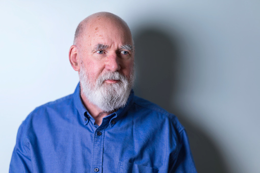 Bald Caucasian man in his 70s with a beard and open-necked blue shirt.
