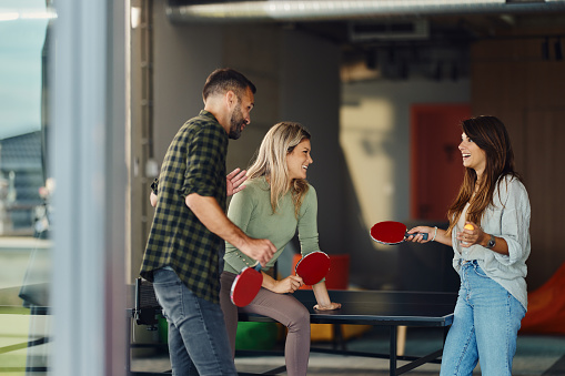 Group of happy colleagues communicating before table tennis game in casual office.