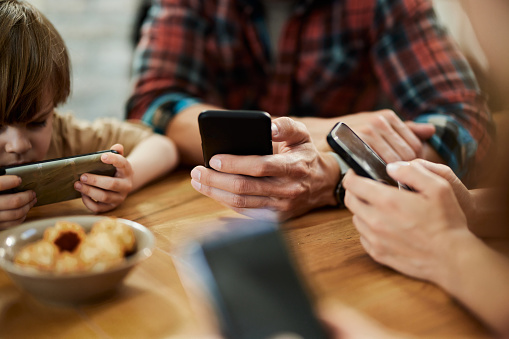 Close up of unrecognizable parents and their small kids using their own cell phones at home.