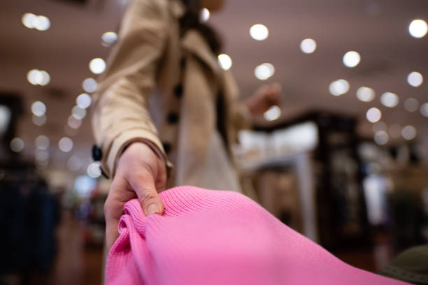 Two beautiful Caucasian women in chic wear, checking the items on a clothing rack. Focus on the girl with blond straight hair, smiling. Side view of the brunette.