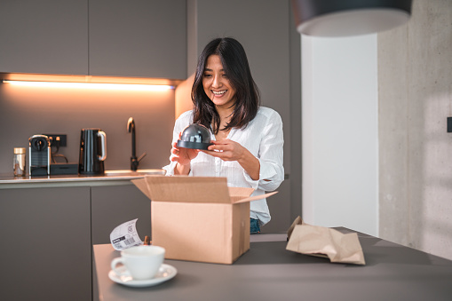 Young Asian female opening a package at home. She ordered an item from an online store. She is wearing casual clothes.