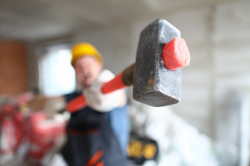 Builder holding a construction hammer at construction site closeup. Master holding sledgehammer for walls concept