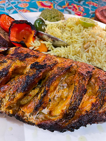 Close up stock photo of a restaurant meal consisting of a tandoori red snapper fish, a grilled fish served with rice and condiments on a white plate at an Indian cafe