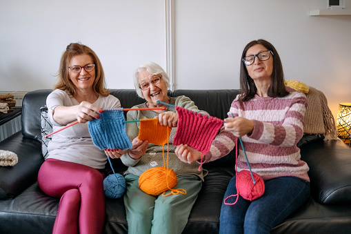 Women having fun with learning how to knit while sitting together in living room