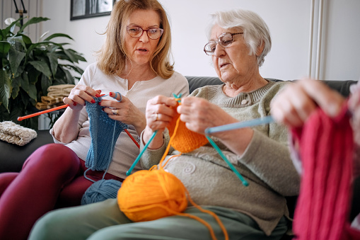 Women having fun with learning how to knit while sitting together in living room