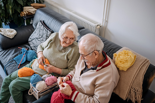 Senior couple knitting at home in living room