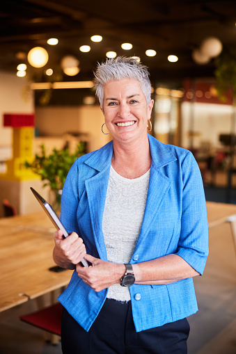 Portrait of a smiling mature businesswoman standing with laptop in the lounge area of a modern office