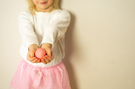 A girl in a pink rock and white shirt holding a pink Easter egg. Happy Easter. Preparation for Easter and spring. High quality photo.
