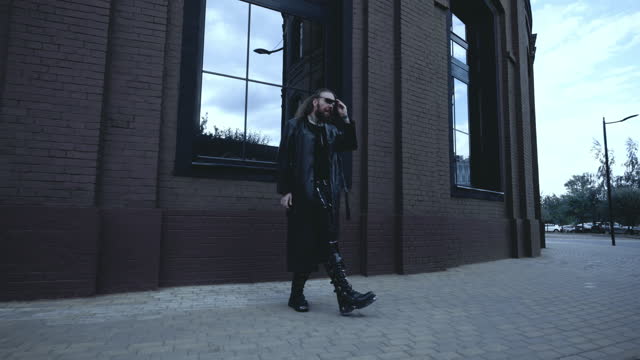 Man In A Black Leather Raincoat Walks Along The Wall