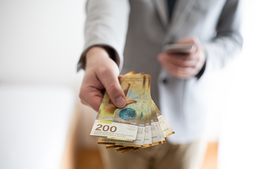 Unrecognizable man in casual suit holding out banknotes of 200 Swiss francs. Close up shot, shallow depth of field, no face.