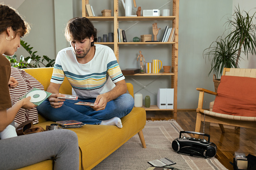 Young couple enjoying at home, checking their old cd's and audio cassettes and enjoying music from the retro cd player