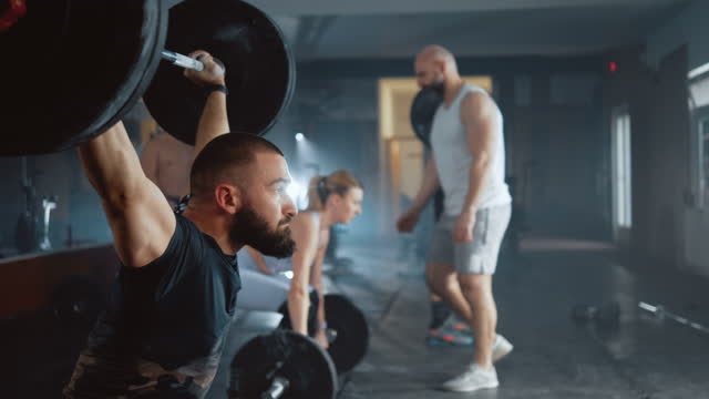 Athletic man lifting a barbell at gym during cross training. Personal trainer shows a group of people how to exercising  with a barbell in the gym.