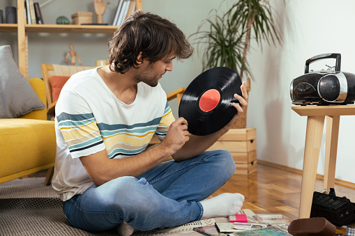 Young man enjoying at home, playing his old cd's and records and enjoying music from the retro cd player