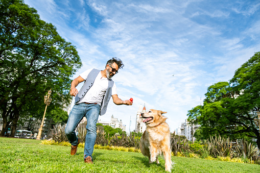 Mature man playing with golden retriever in public park