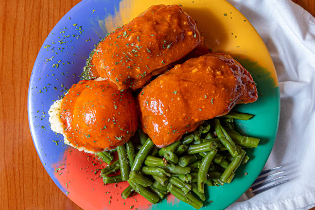Partly sliced piece of stuffed fish carp before serving, made from a mixture of ground deboned carp with carrot stuffed inside the intact fish skin on a white dish on a gray background