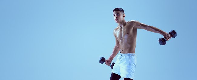 Portrait of young muscular man training with dumbbells isolated over blue background in neon light. Flyer. Concept of sport, fitness, healthy and active lifestyle, motivation, workout
