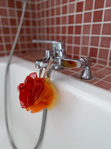 Red, orange and yellow colored bath sponge hanging from the faucet in the bathtub