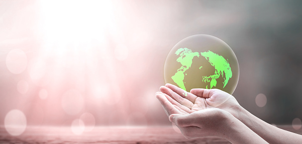 Earth day concept, A green earth globe in human hands over blurred beautiful nature background