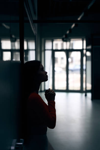 istock Sad female corporate worker praying in dark empty office corridor 1474164599