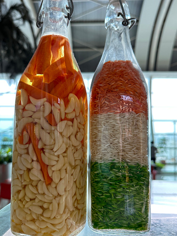 Stock photo showing two glass bottles, one is full of garlic and chilli pepper oil being marinaded, the other is full of rice in the colour of the Indian flag, green, white and orange