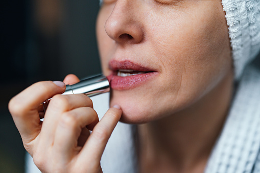 An anonymous woman in bathrobe putting make up while sitting in the bedroom in the morning.