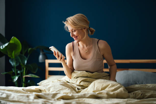 istock Happy Woman Using A Mobile Phone In The Bedroom 1474168330
