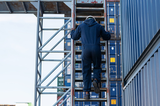 Excellent quality control and inspection make customer confident. African Dock engineer worker climb the ladder to inspector the quality of container box in the container warehouse yard. Logistic import and export industrial