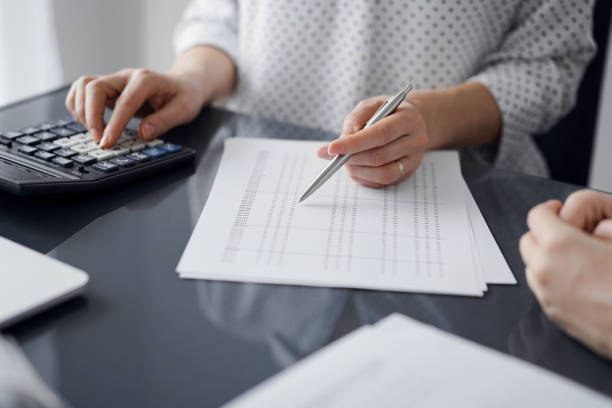 istock Woman accountant using a calculator and laptop computer while counting and discussing taxes with a client. Business audit and finance concepts 1474169872