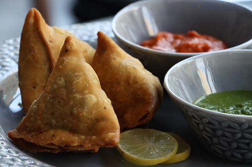 Stock photo showing samosas stuffed with spiced potato, peas and meat served with bowls of tomato chutney and mint and coriander dipping sauce. These popular Indian snack is often sold by street food vendors.