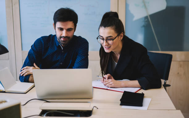 istock Positive coworkers working with program on laptop and writing down comments in notebooks 1474175101
