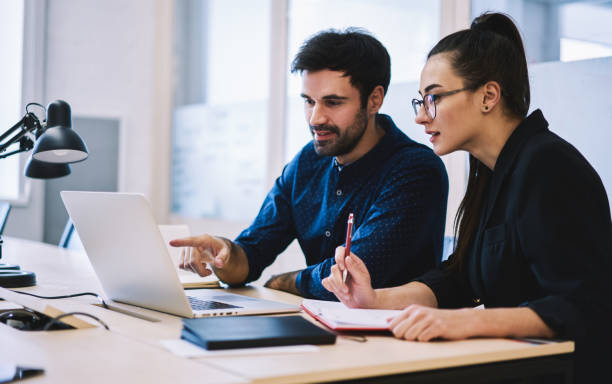 istock Smiling colleagues preparing report together working on laptop 1474175106