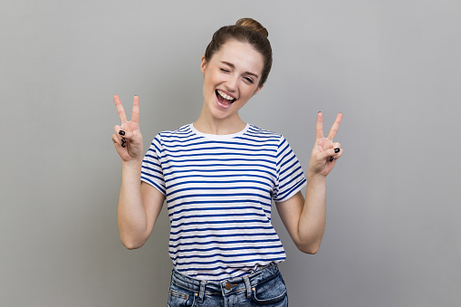 Redheaded young woman making victory sign with her hand and smiling. Blurred background.