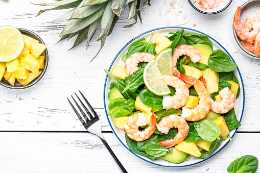 Fresh pineapple shrimp salad with spinach, avocado and lime on white wooden table, top view. Healthy eating, balanced, clean diet food