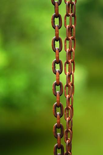 Close up shot on rusty heavy metal chains against blurred green background.
