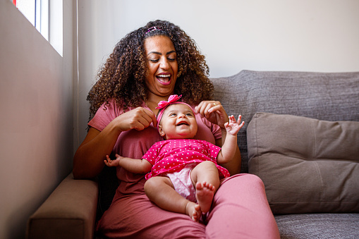 cheerful woman resting on sofa with her baby daughter on her lap