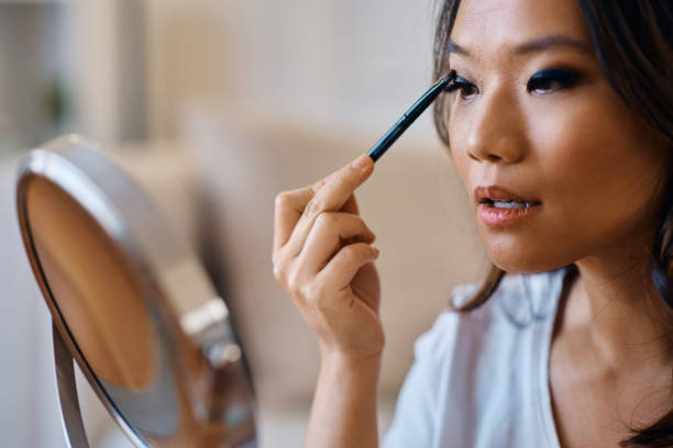 istock Young Asian woman applying eyeshadow while doing makeup at home. 1474183310