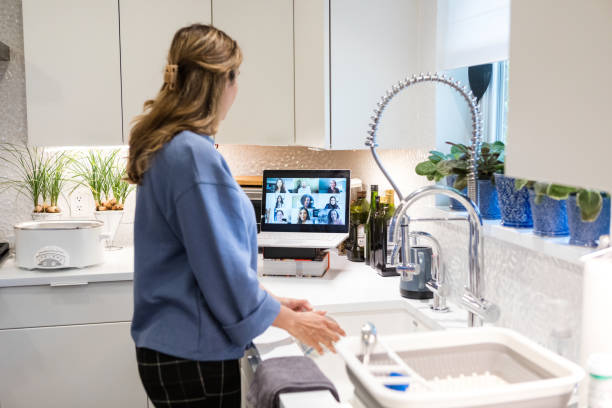 Businesswoman teleconferences with colleagues while washing dishes at home