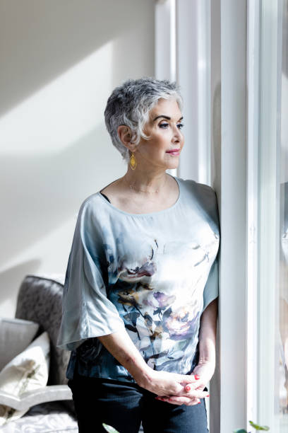 istock Senior woman stands looking out window 1474183400