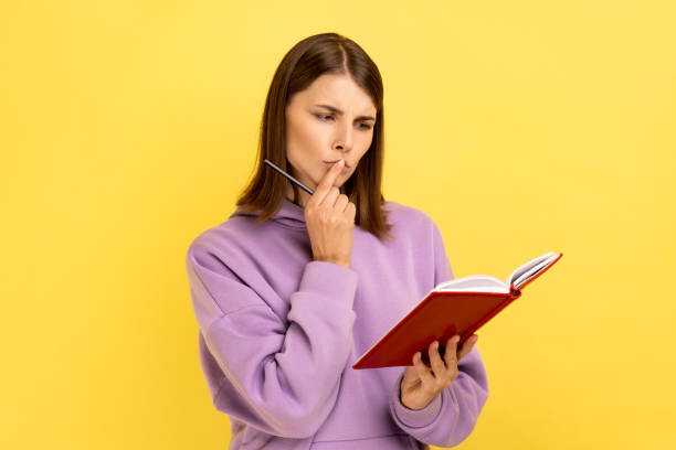 istock Woman standing with paper notebook and pen, looking away with pensive expression, making to do list. 1474184904