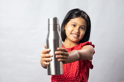 An Indian asian girl child in red dress with a stainless steel bottle of water on white background