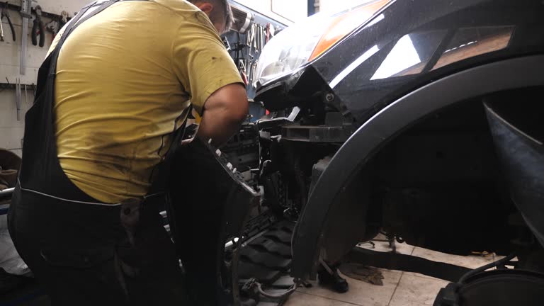 Two mechanics removing front bumper from car for repair in auto service. Professional repairmans dismantling automobile before fix at workshop or garage. Concept of vehicle maintenance and diagnostic