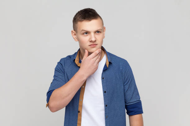 serious teenager guy wearing shirt looking away, holding chin, thinking about future plans, planning - pensive question mark teenager adversity imagens e fotografias de stock