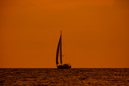 Silhouette of a sailing boat in sunset sunrise time and ocean horizon.