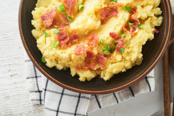 istock Mashed boiled potatoes. Bacon mashed potatoes with green onion, pepper and cheddar cheese in bowl on light old wooden backgrounds. Delicious creamy mashed potatoes. Top view. 1474187086