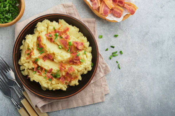 istock Mashed boiled potatoes. Bacon mashed potatoes with green onion, pepper and cheddar cheese in bowl on light old wooden backgrounds. Delicious creamy mashed potatoes. Top view. 1474187693