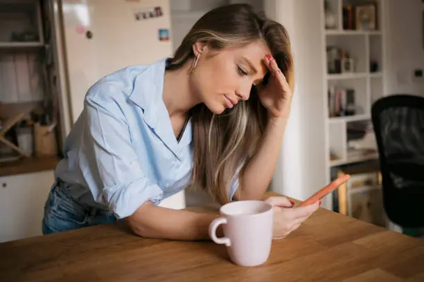 Photo of Young woman using her cellphone while drinking coffee in kitchen