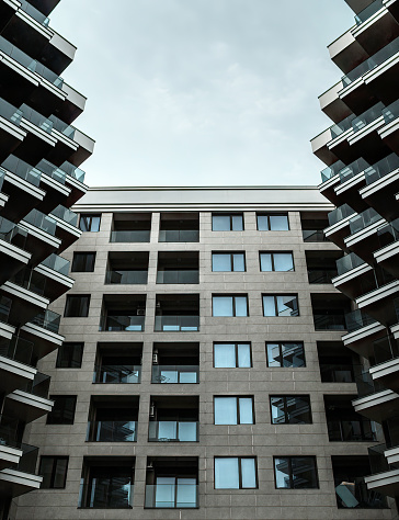 Low angle view of facade through buildings on sides, with angular balconies with glass railings.