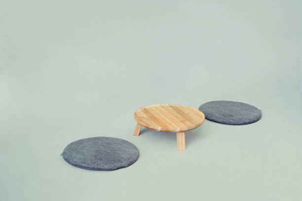 Japanese-style round table with seat cushions On a clean gray floor, there is a small Japanese-style round table and two dark gray round seat cushions. The minimalistic design and neutral color scheme create a peaceful and serene atmosphere. zabuton stock pictures, royalty-free photos & images