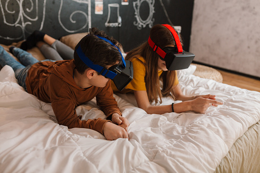 Teenagers watching media on virtual reality glasses in the bederoom