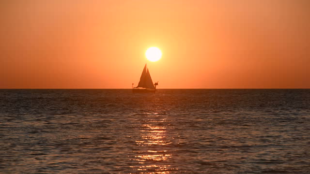 Sailing Into Sunset - A small sailboat sailing in front of setting sun and orange sky on an Autumn evening. Clearwater, Florida, USA.